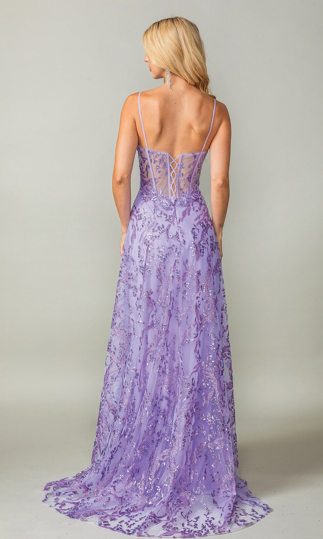 A woman with long blonde hair models the Dancing Queen 4402, a lavender long glitter-print prom dress with sequin details, thin straps, and a lace-up back, standing against a plain background.